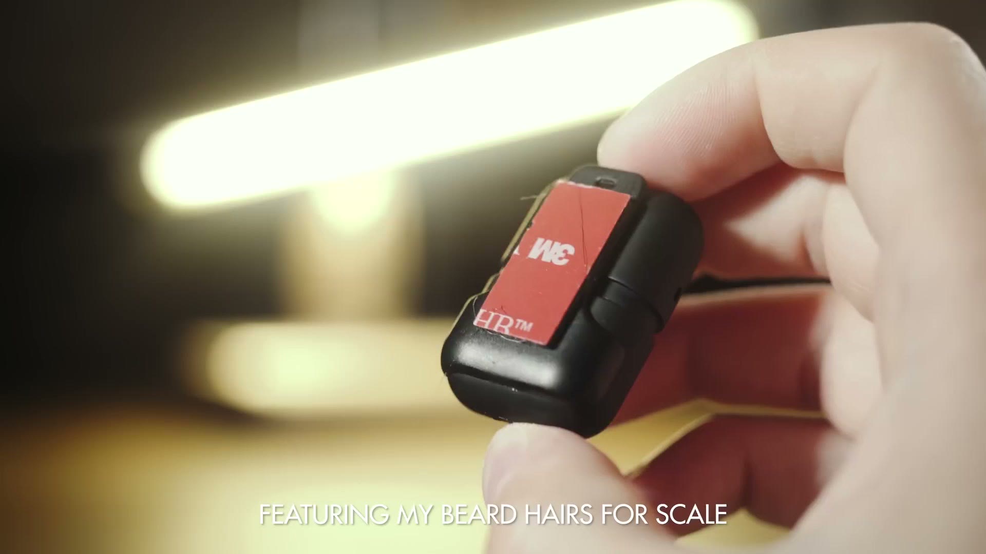 A hand holding the Instamic with a 3M adhesive quick release mount attached to its back