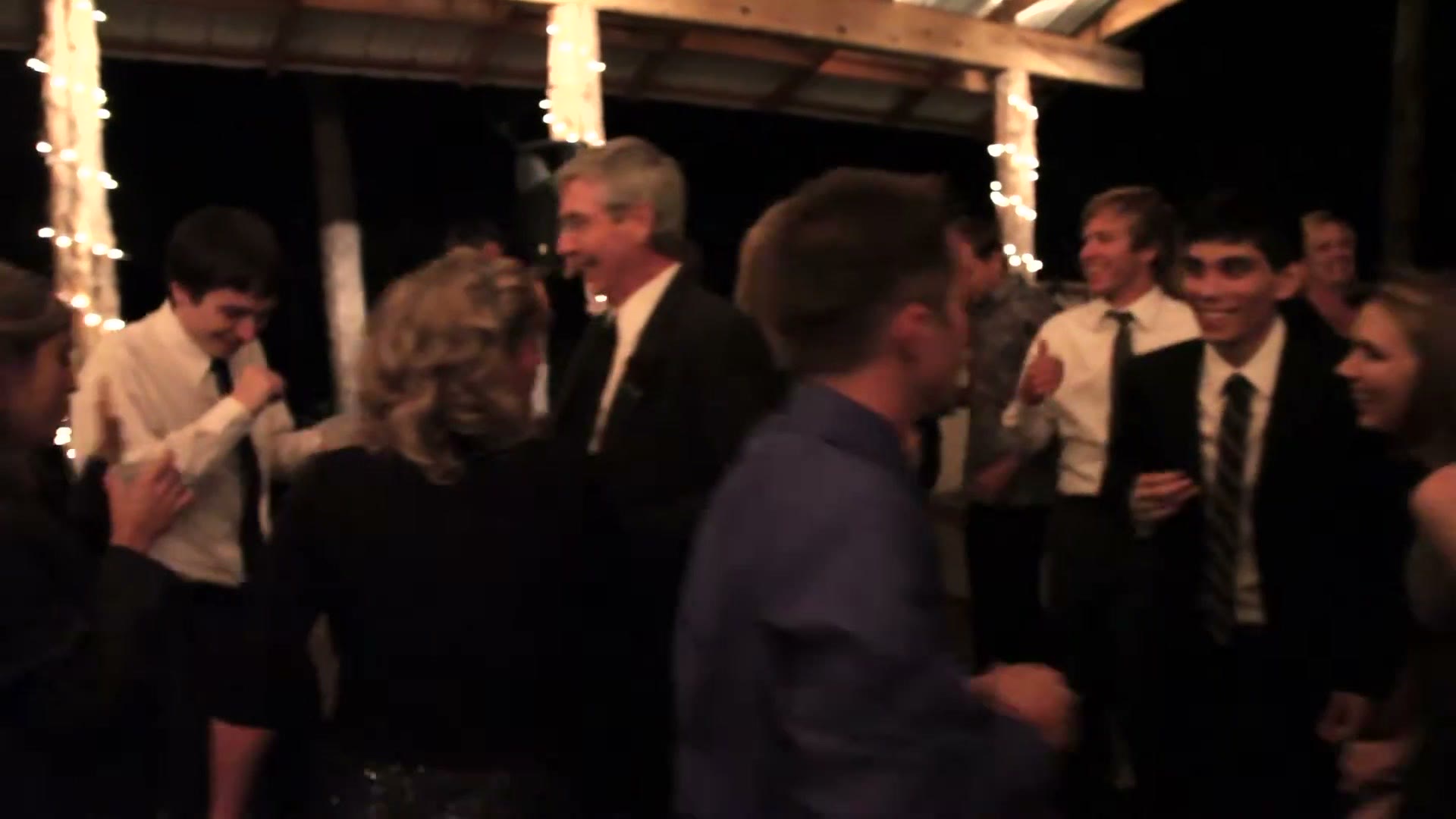 Wedding guests dancing under an open timber pavilion lit by strings of fairy lights after dark