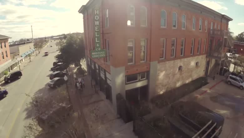 A drone view circling a red brick building in downtown Bryan with Howell & Co Wholesale Grocers painted down its side