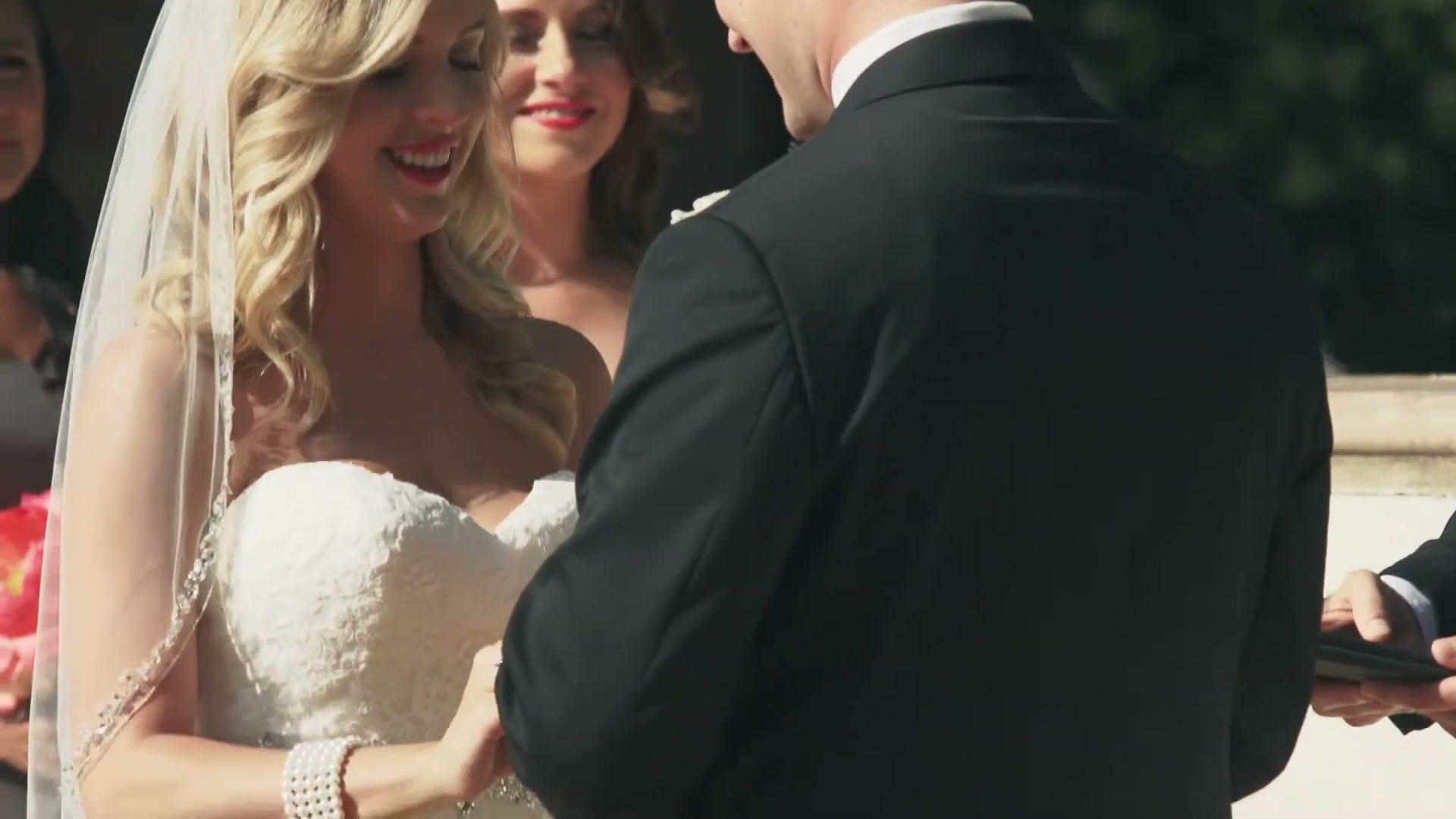 The bride laughing during the ring exchange while the groom works at her hand, a bridesmaid grinning behind them