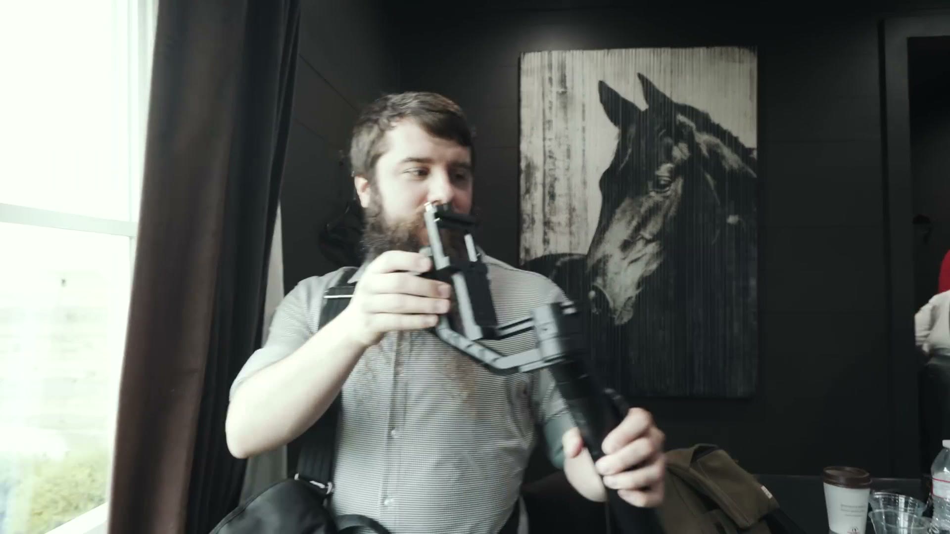 Matt holding up a handheld electronic gimbal in the groom's suite while the groomsmen finish getting dressed behind him.