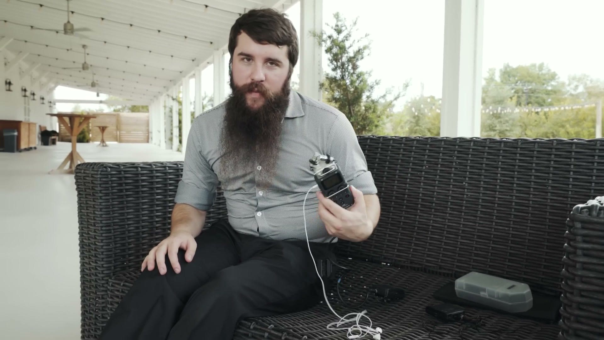 Matt sitting on an outdoor sofa holding a Zoom H5 audio recorder with a cable running out of it.