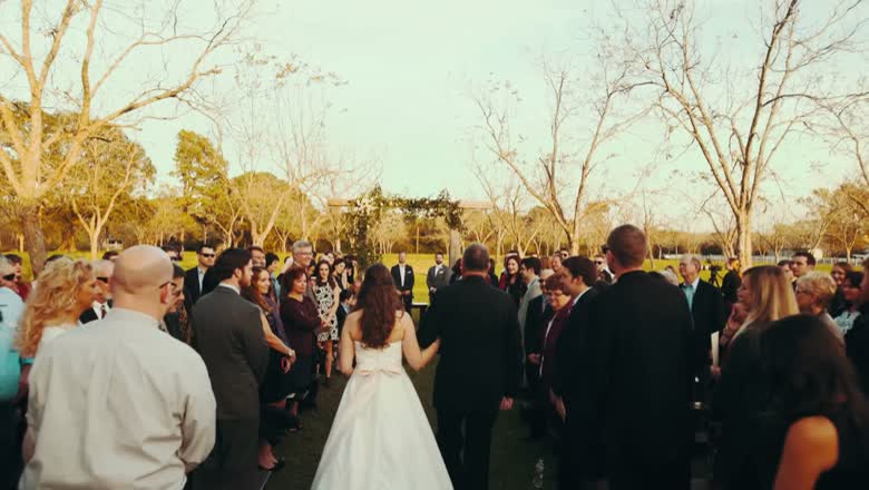 The couple walking back down the aisle between standing guests, with bare winter trees and open lawn behind