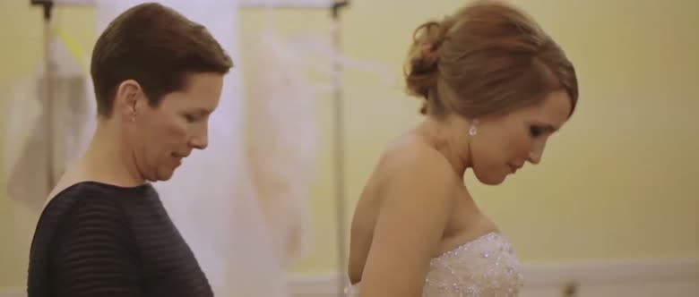 The bride in her beaded gown standing with her mother, both looking down as the dress is adjusted