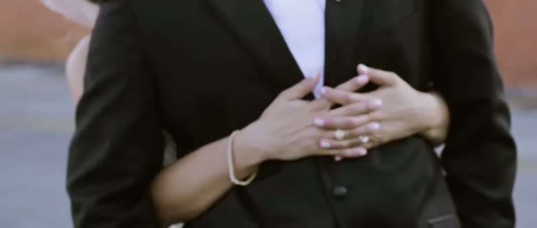 The bride's hands folded over the groom's chest, both wedding rings visible against his dark suit