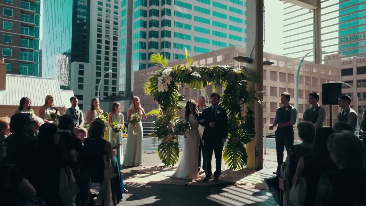 The couple at the altar under a palm frond arch with downtown towers behind them