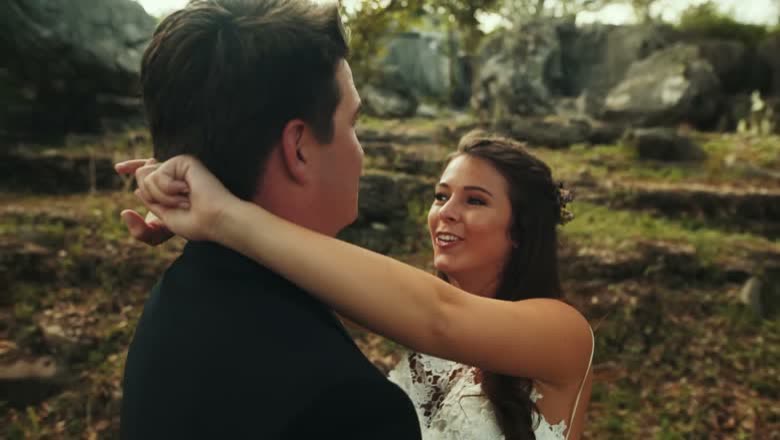 The bride laughing with her arm around the groom's neck out among limestone outcrops and scrub on the ranch