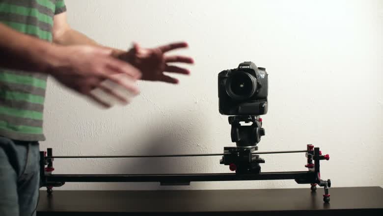 A DSLR mounted on the Master Pan on a slider set up on a table top, being pushed through a slide and pan move by hand