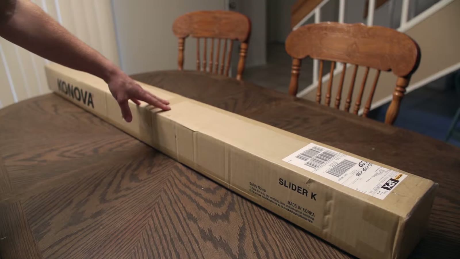 Fingers resting on top of the sealed Konova Slider K box, ready to tear the packing tape