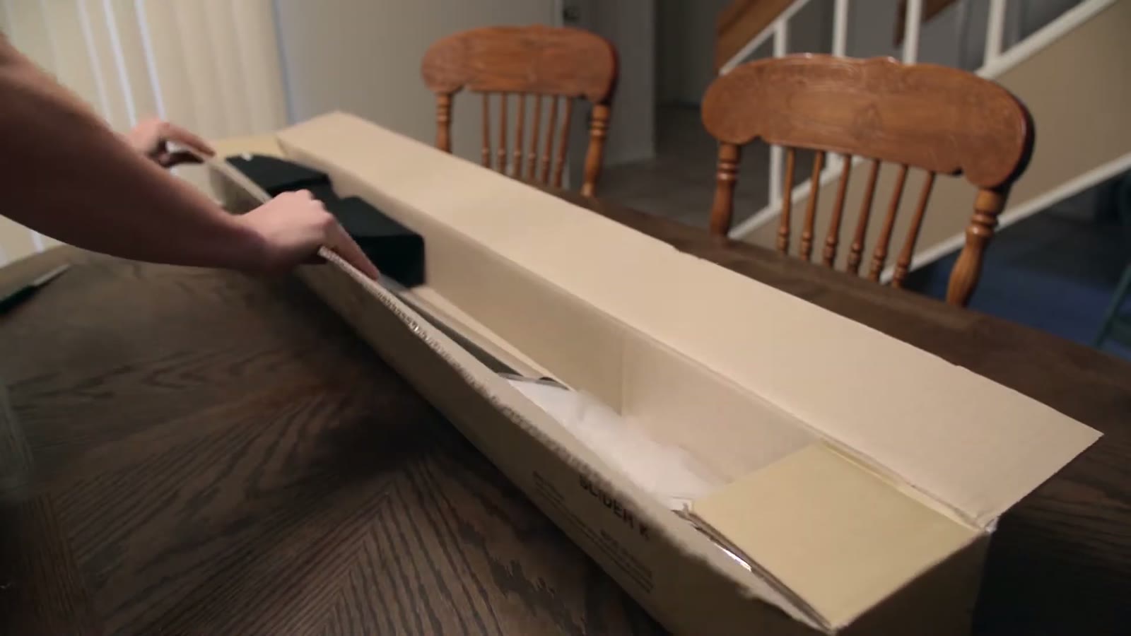 Both hands lifting the flap open on the Konova box, foam padding and a dark component visible inside