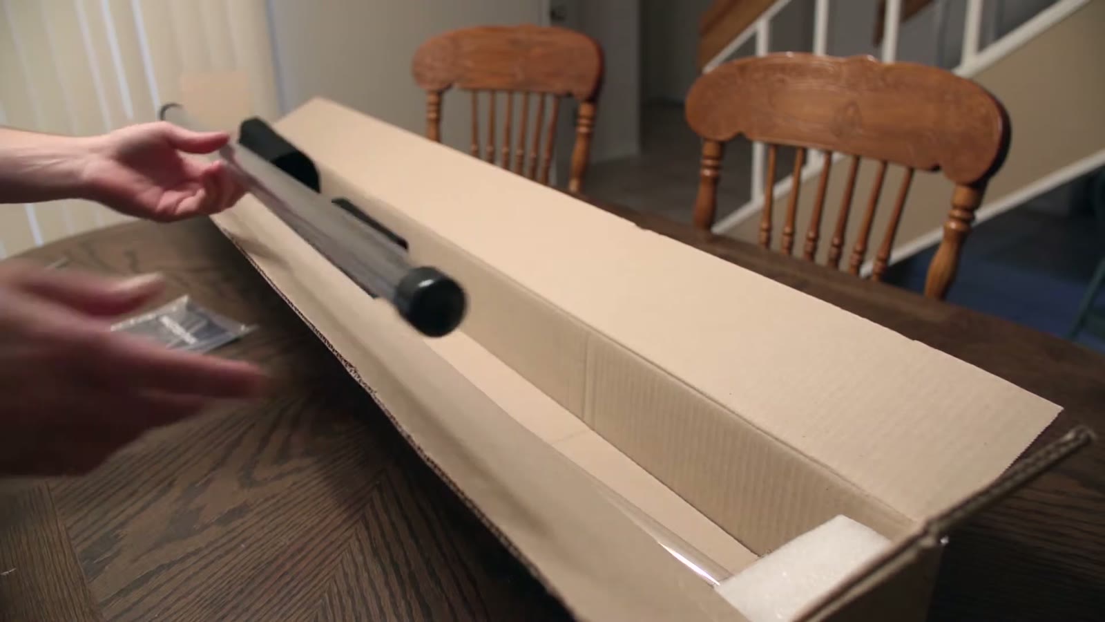 Hand reaching for a black cylindrical slider rail cushioned in foam inside the open Konova box