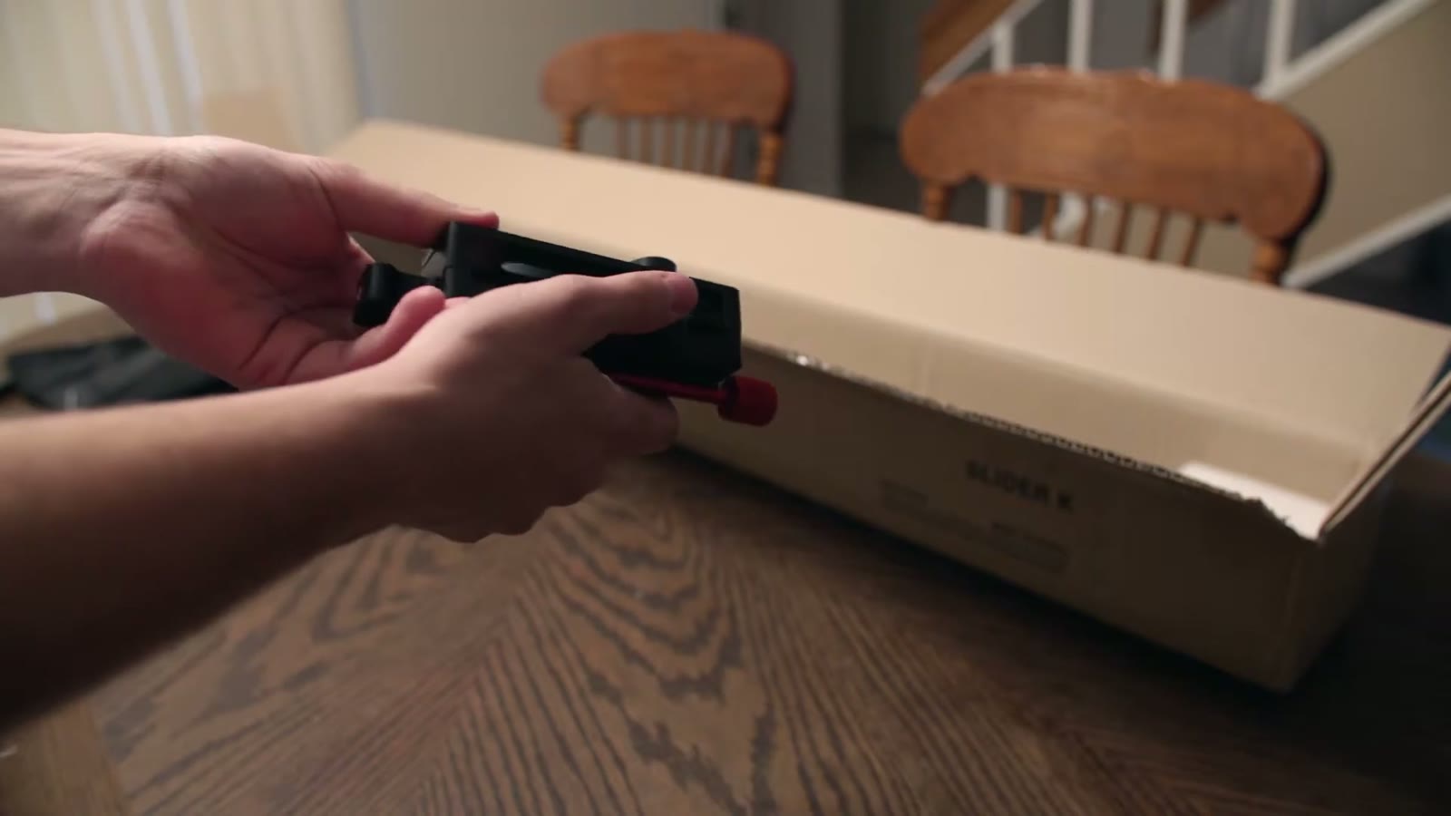 Two hands examining a black bracket with a red locking knob pulled from the slider box