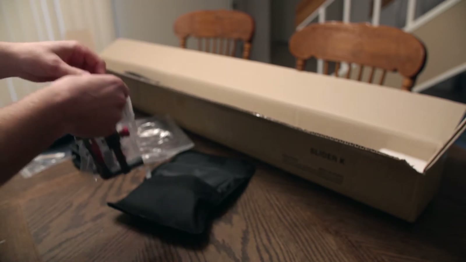 Hands unwrapping a small plastic bag of hardware next to a black pouch and the open slider box