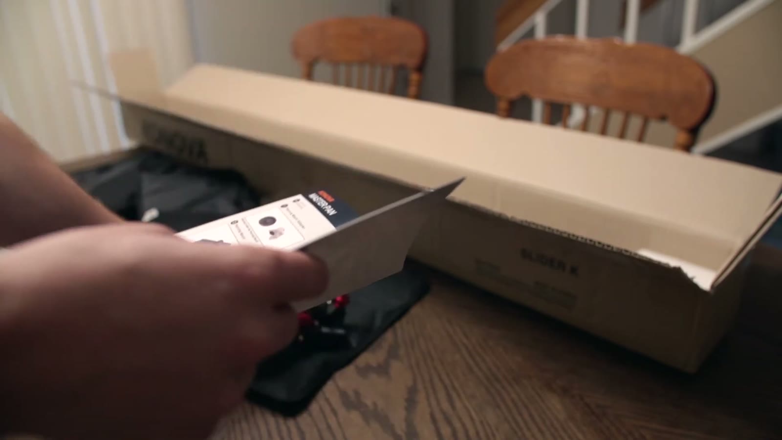 Hand unfolding a printed instruction sheet in front of the slider box, a small plastic-wrapped part below