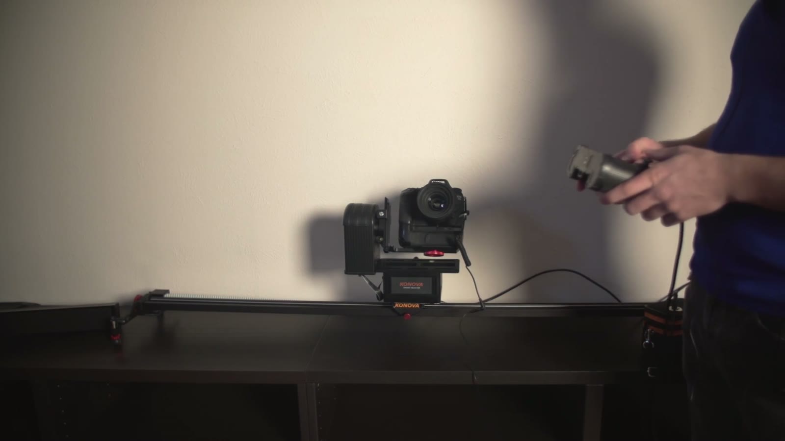 Camera and Smart Head mounted on a slider rail on a table, man holding a wired remote control to the side