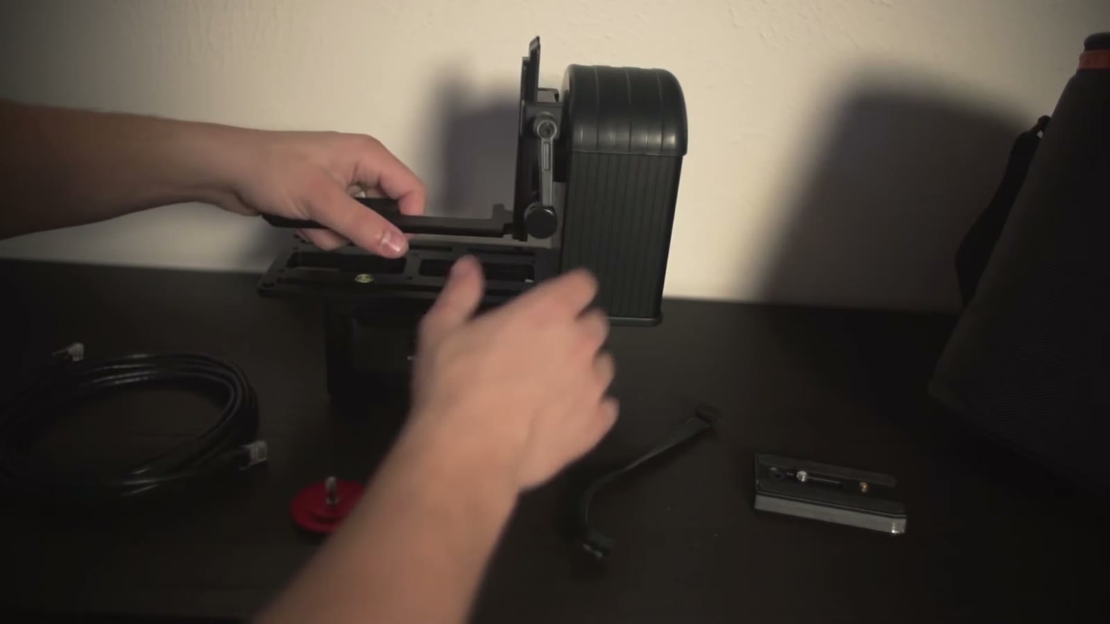 Hands assembling the Smart Head base with a cable, red mounting knob, and small bracket laid out nearby