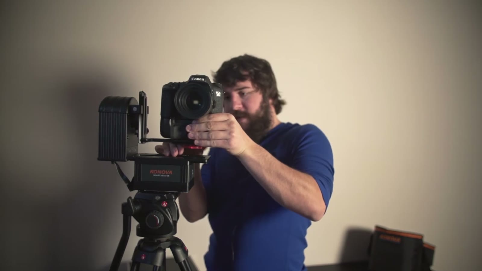 Man in a blue shirt looking through the Canon camera mounted on the Konova Smart Head on a tripod
