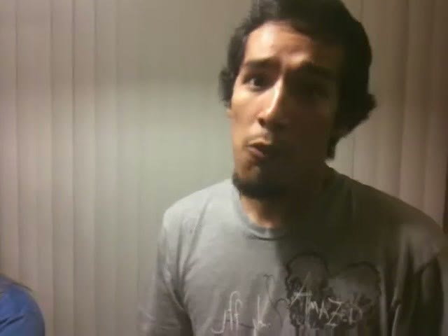 A young man talking directly to the handheld camera in a dim apartment, mid sentence, the footage soft and grainy