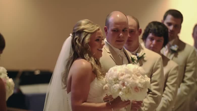 The bride laughing beside the groom and his groomsmen, all in cream suits, holding a large white bouquet