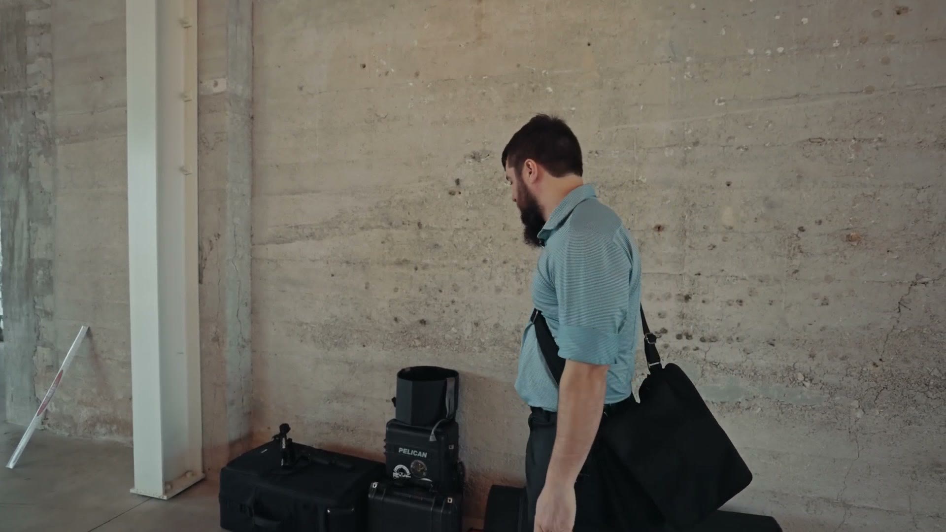 Matt carrying gear cases toward a light stand in an empty reception hall