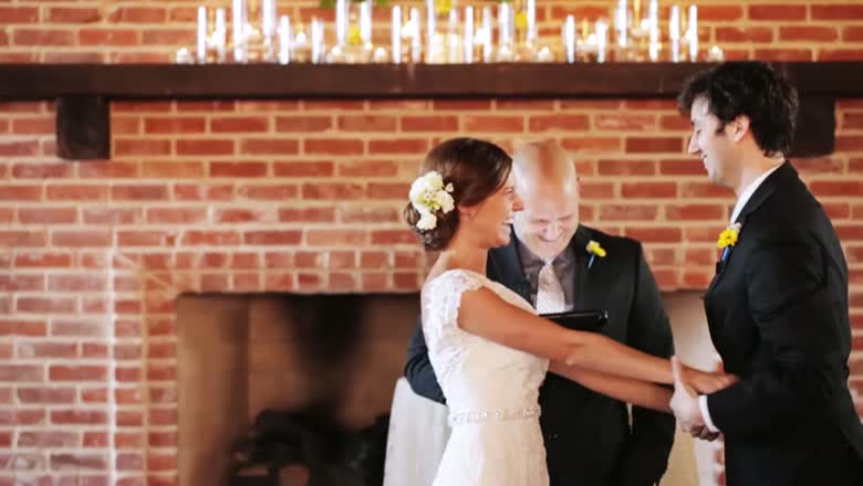 The couple holding hands in front of the minister at a brick fireplace lined with tall candles
