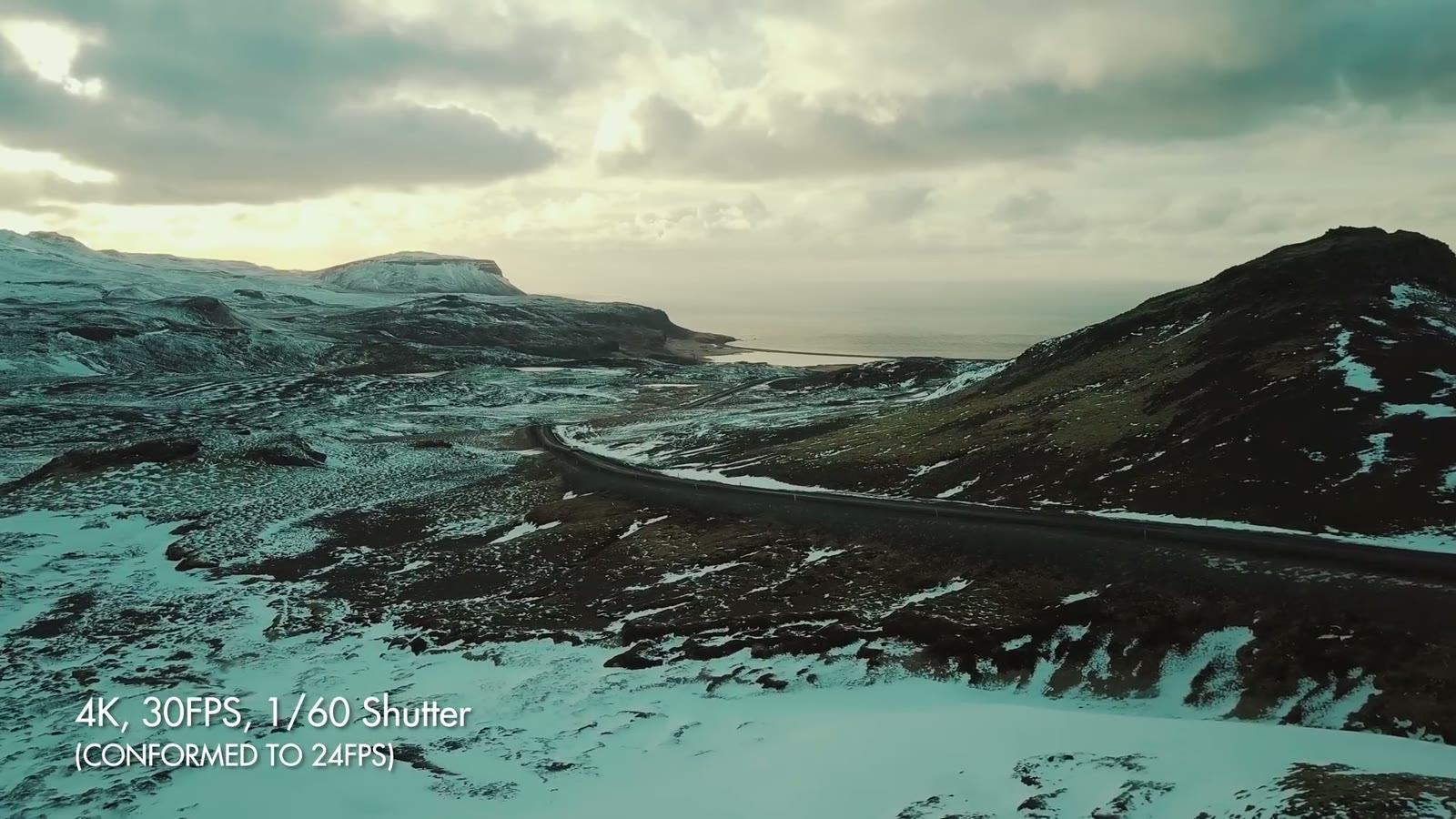 An aerial of a mountain road along a coastline, labelled 4K 30FPS 1/60 shutter, conformed to 24fps