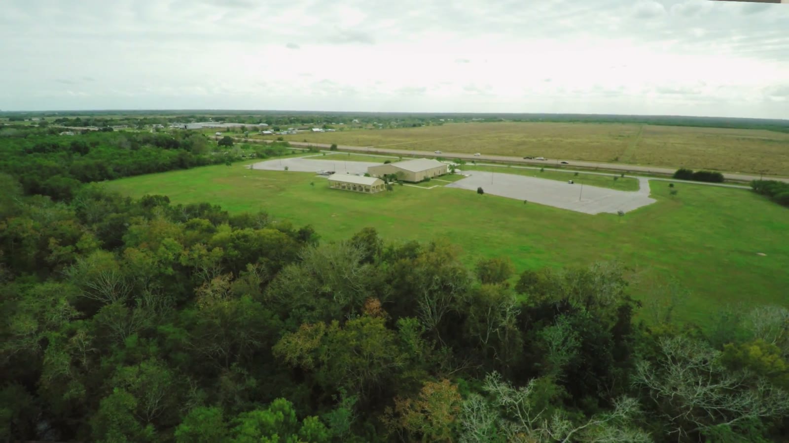 Aerial drone view of a South Texas wedding venue surrounded by trees, with a highway and open fields beyond