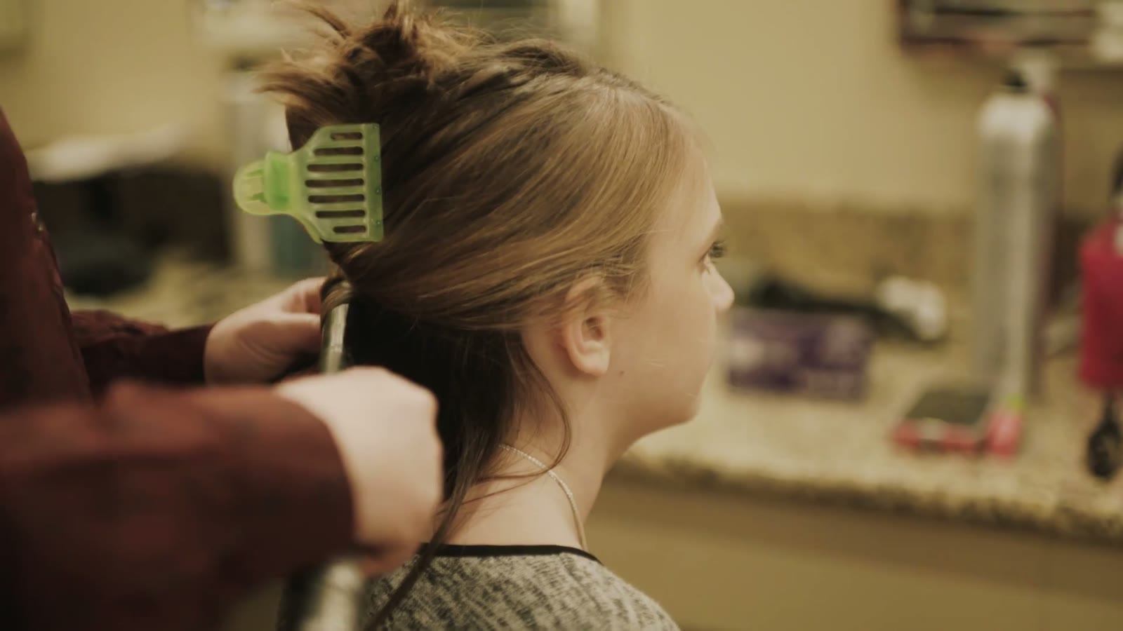 Stylist curling a young bridesmaid's hair with a green clip holding back the top section