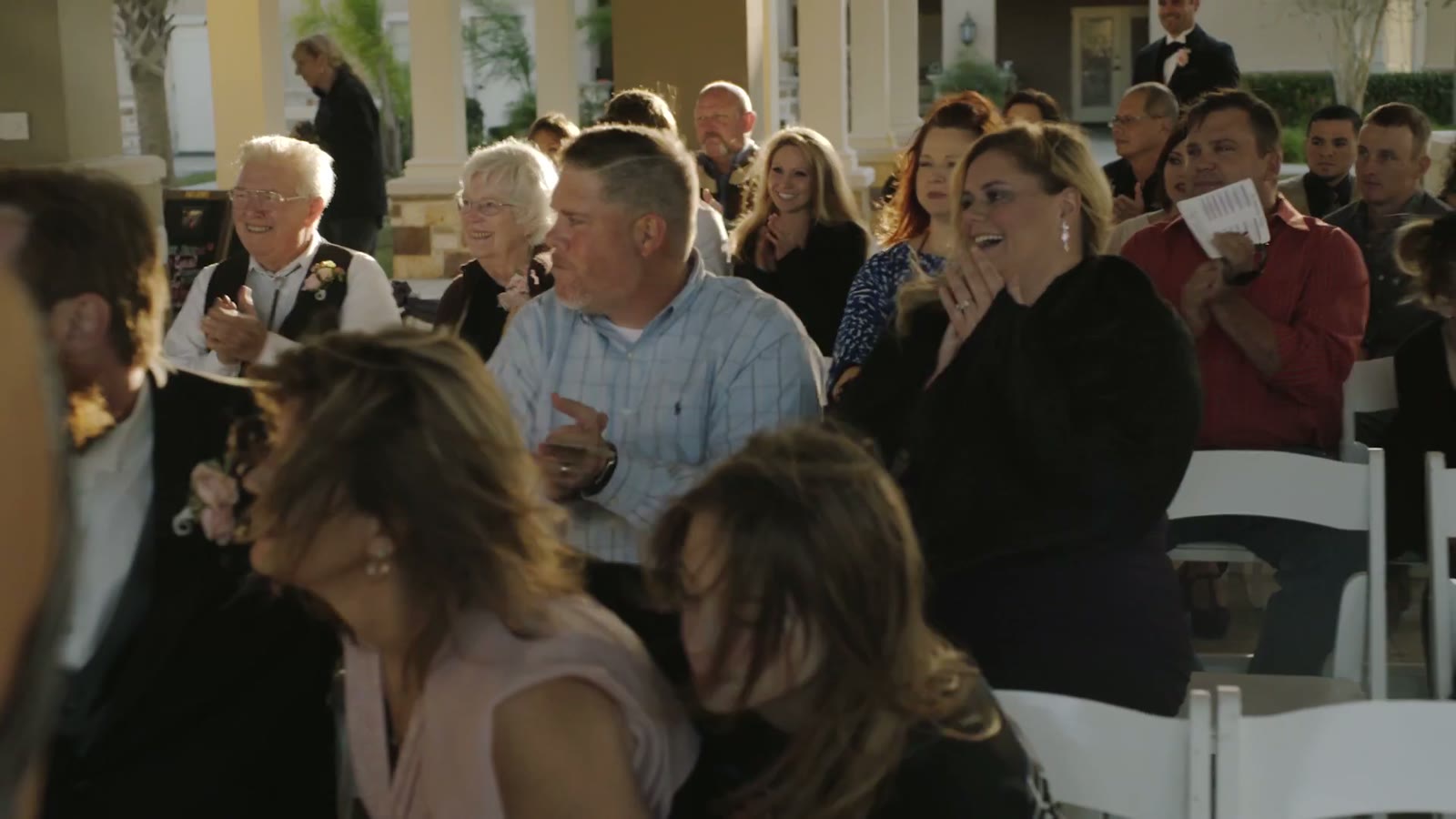 Wedding guests seated outdoors clapping and smiling during the ceremony