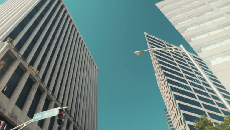 Looking straight up at downtown Nashville high rises against a bright blue sky, with a street sign in the corner of frame