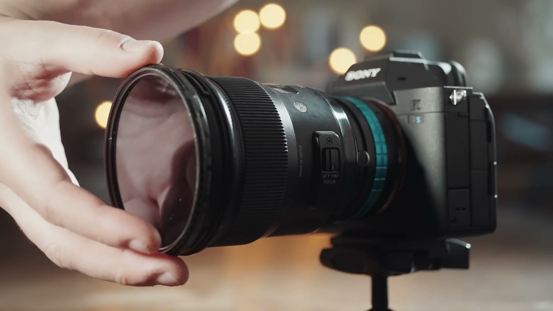 A hand bringing a round filter up to the front of a lens on a Sony camera, held only by magnets
