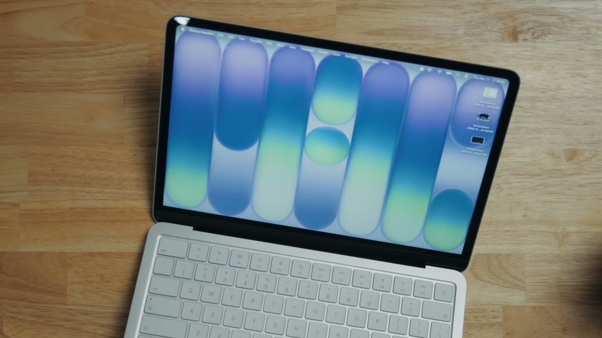 MacBook Neo open on a wooden desk showing a colorful macOS wallpaper