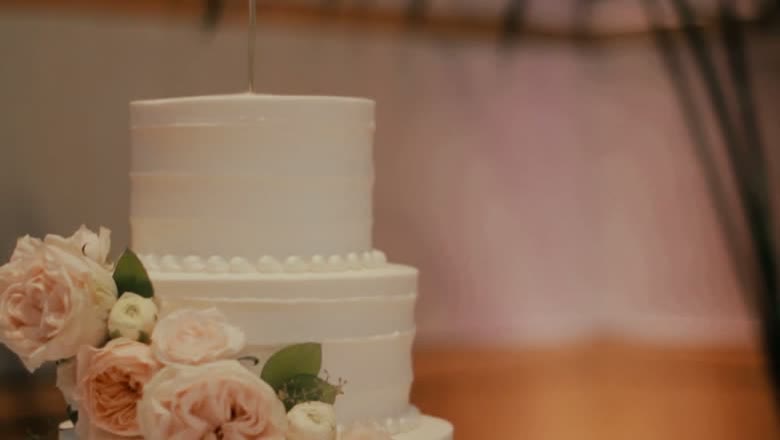 A tiered white wedding cake with pale roses and greenery arranged at its base