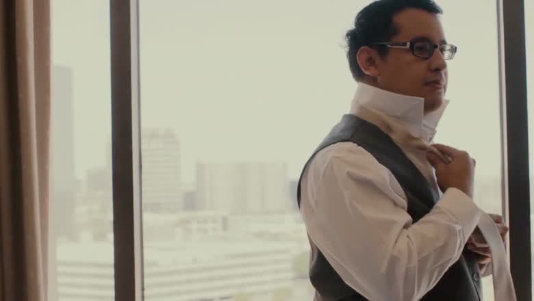 The groom fastening his collar at a floor-to-ceiling window with the city skyline behind him