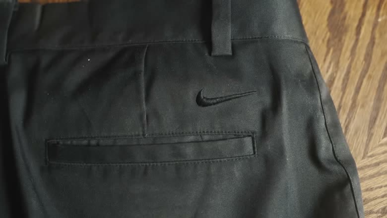 Close-up of a pair of black Nike golf pants laid flat on a wooden floor, with the swoosh embroidered on the back pocket