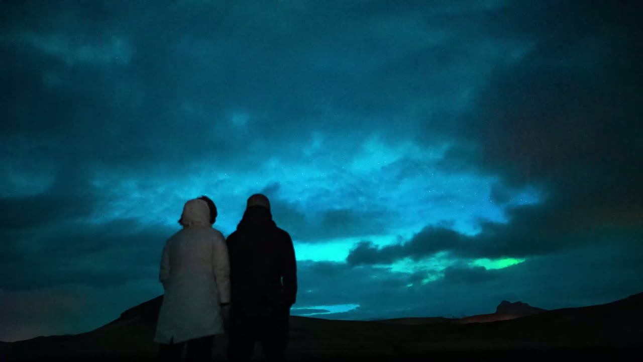 Silhouette of a couple watching green northern lights glow across a night sky