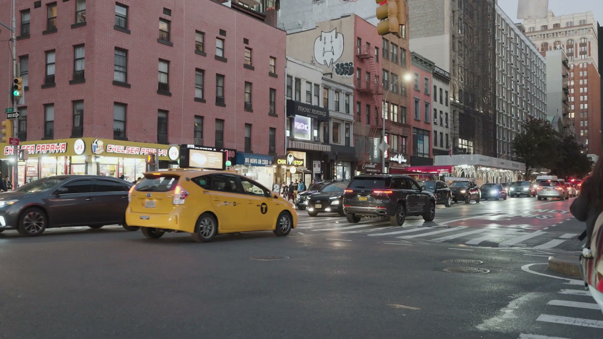 A New York City street at twilight with a yellow taxi and traffic