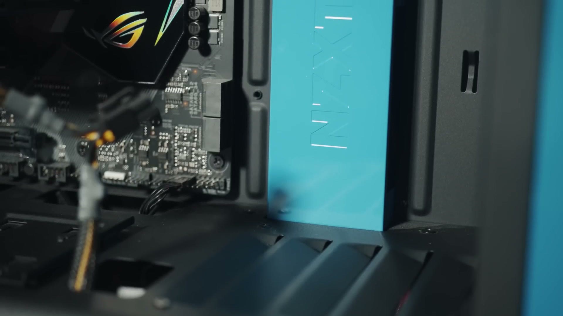 Close-up inside the NZXT case showing the teal PSU shroud panel next to the ROG motherboard heatsink