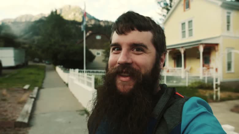 Walking a small Colorado mountain town street past a yellow clapboard house with peaks rising behind the rooftops