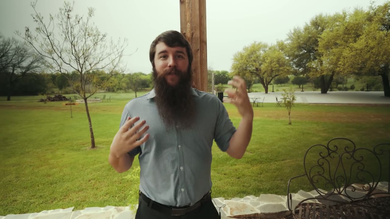 Matt talking to camera on a porch with a green field and scattered trees behind him