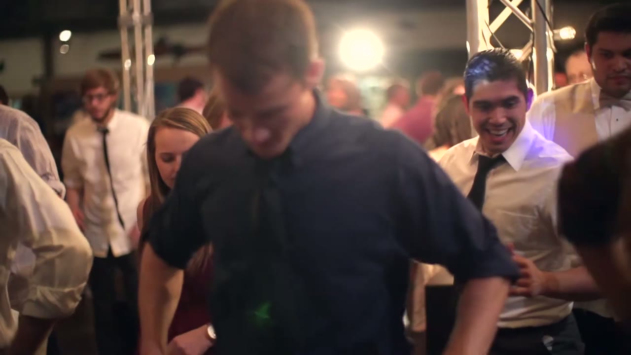 Close crowded shot of guests dancing, a man in a loosened tie mid-move in the foreground