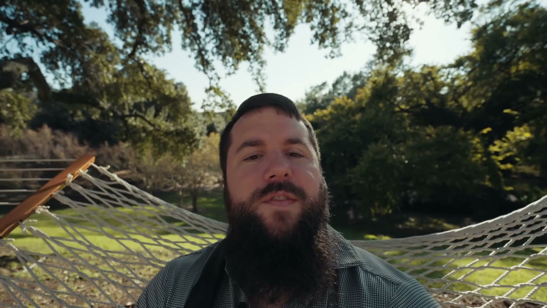 Matt lying back in a rope hammock among oak trees with the wedding lawn behind him