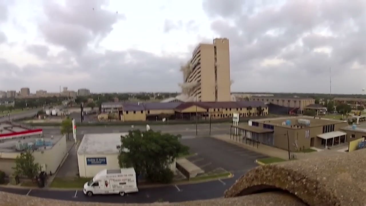 An elevated wide view of the collapsing tower with a car park, a low motel and the surrounding town spread out below it