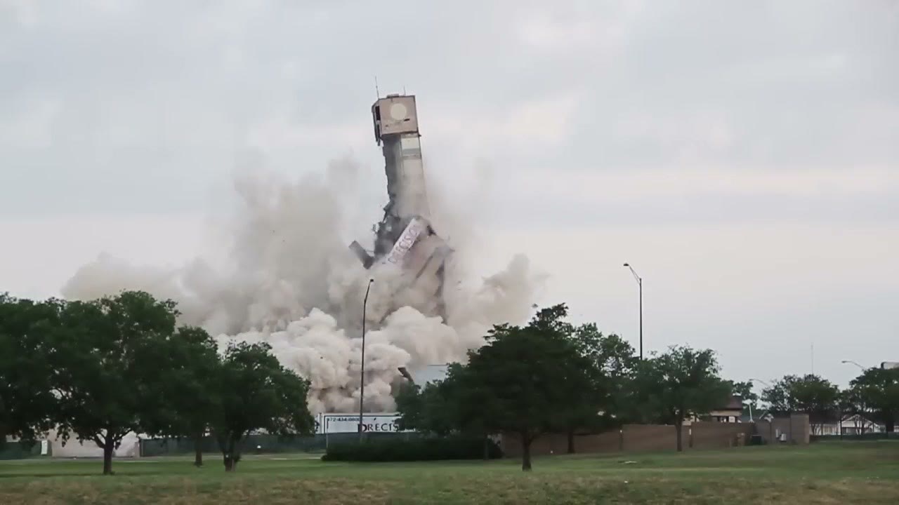 The upper section of the hotel tower toppling sideways out of a rising cloud of dust during the implosion