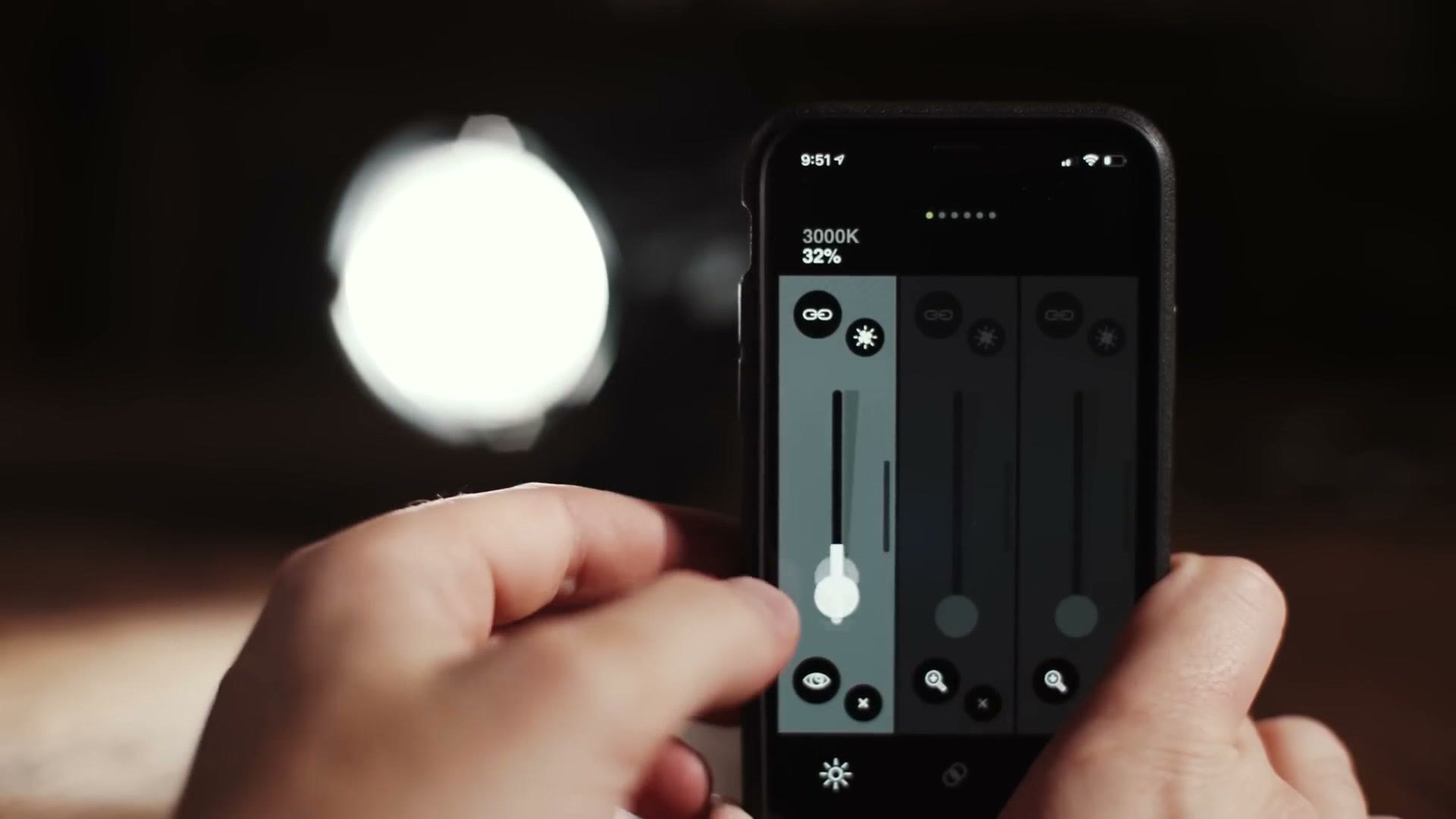 A phone running the Practilite remote control app showing 3000K at 32 percent, held next to the lit Practilite 602