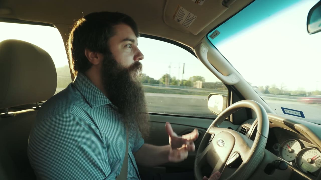 Matt talking and gesturing from the driver's seat while driving on the highway to the wedding