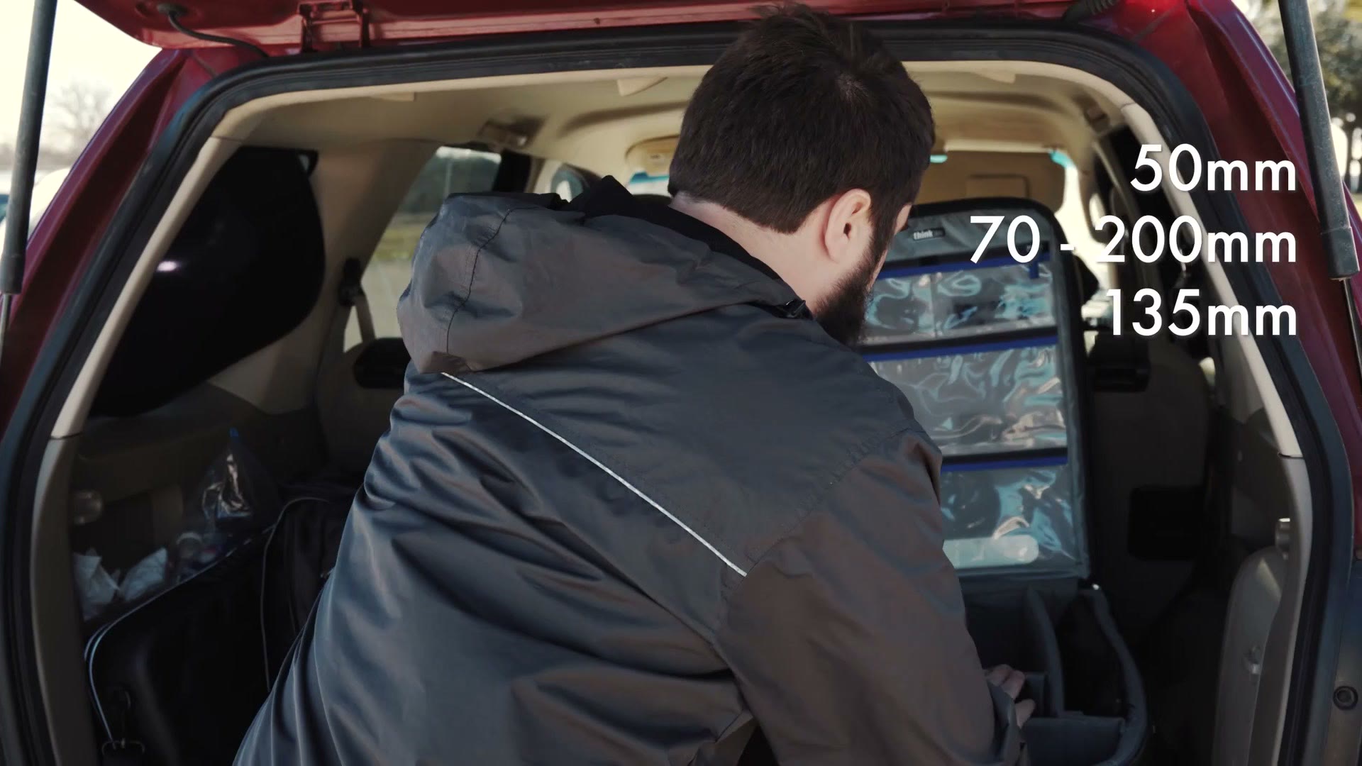 Matt leaning into the back of an SUV over an open camera case, with on-screen text listing 50mm, 70-200mm and 135mm.