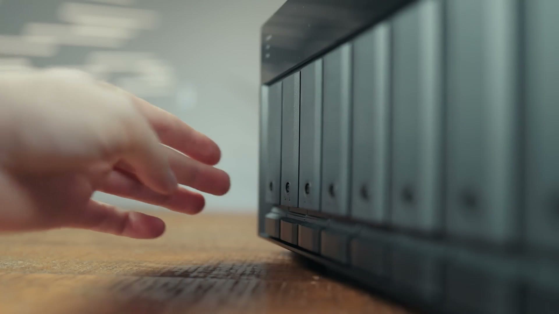 A hand reaching toward the eight drive bays on the front of the QNAP NAS