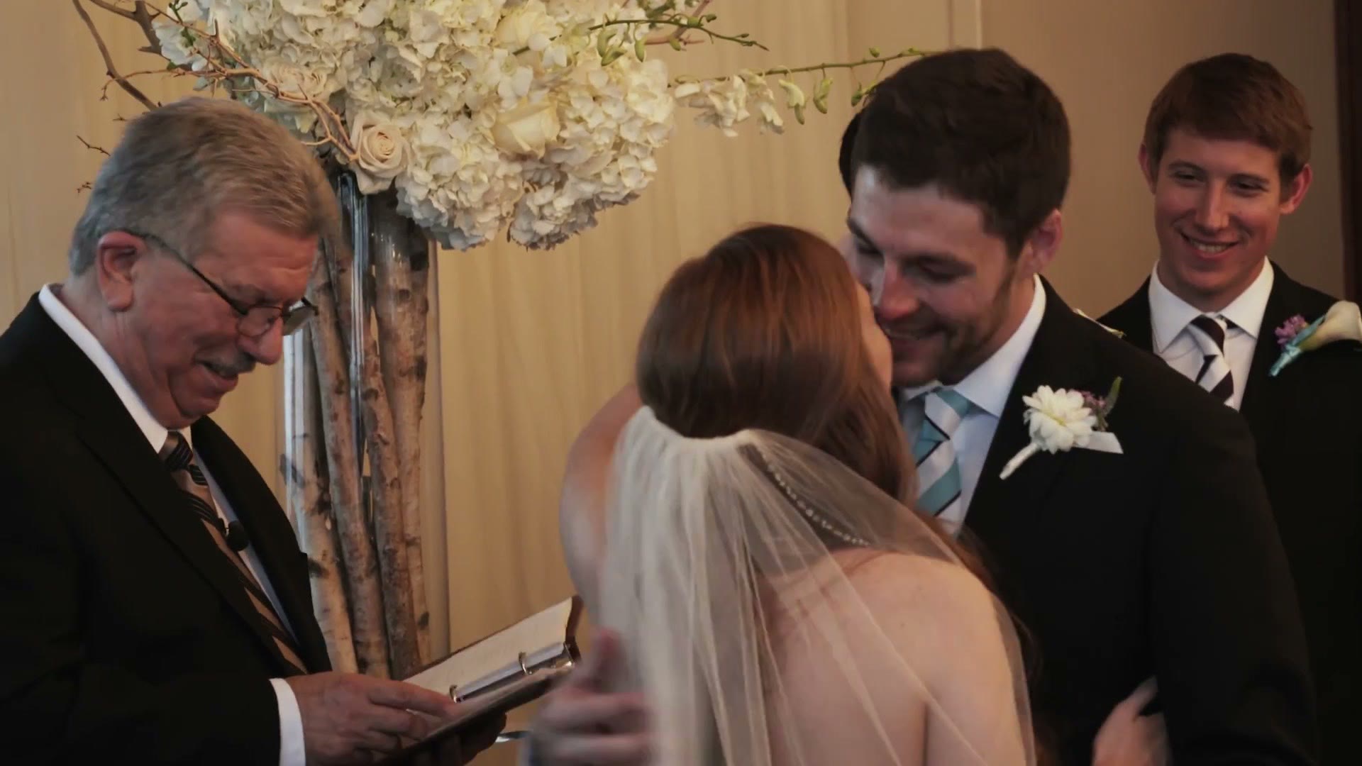 Officiant reading from a book at the altar as the bride and groom face each other, groomsman smiling behind