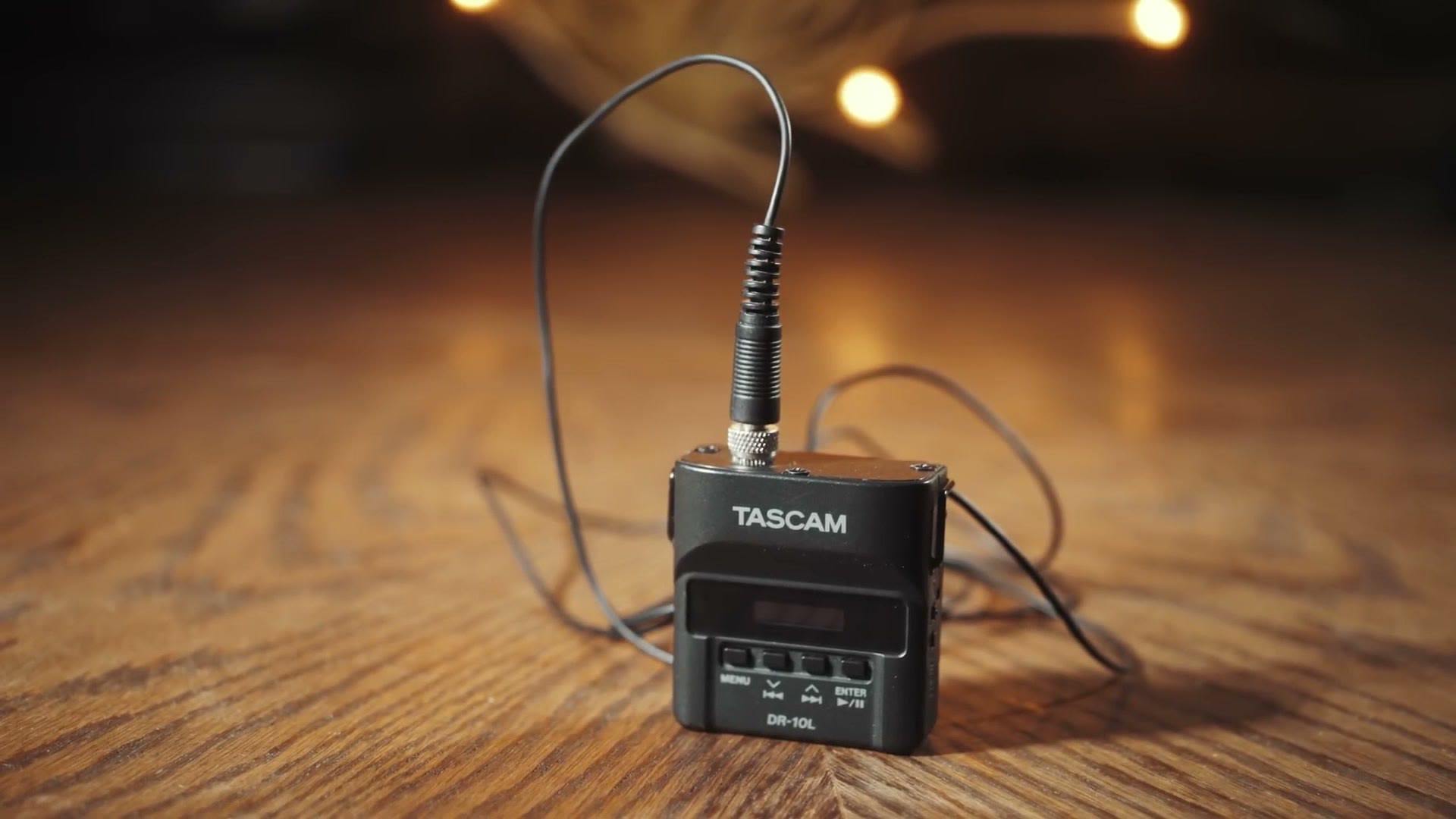 A Tascam DR-10L recorder on a wooden table with a lav mic plugged into the top
